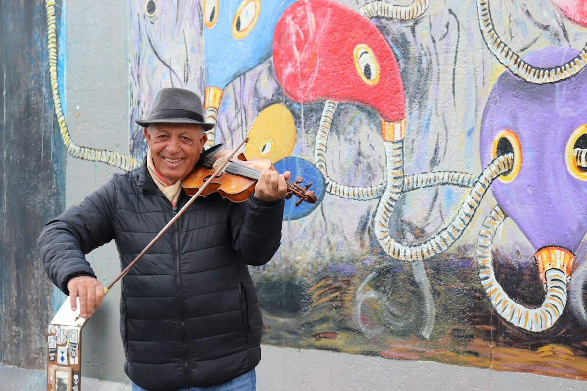 A smiling violinist performs in front of a colorful mural